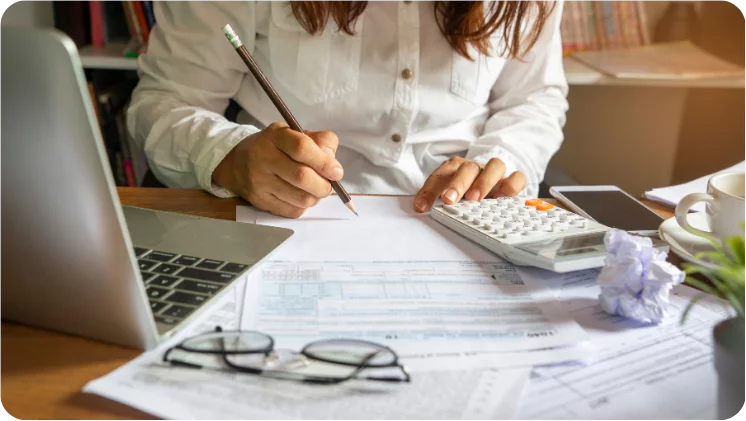 Woman using a calculator while making notes on a budget plan